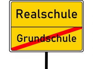Gelbes Schild, wie es am Ortseingang und -ausgang steht. Oben das Wort "Realschule", unten rot durchgestrichen das Wort "Grundschule".