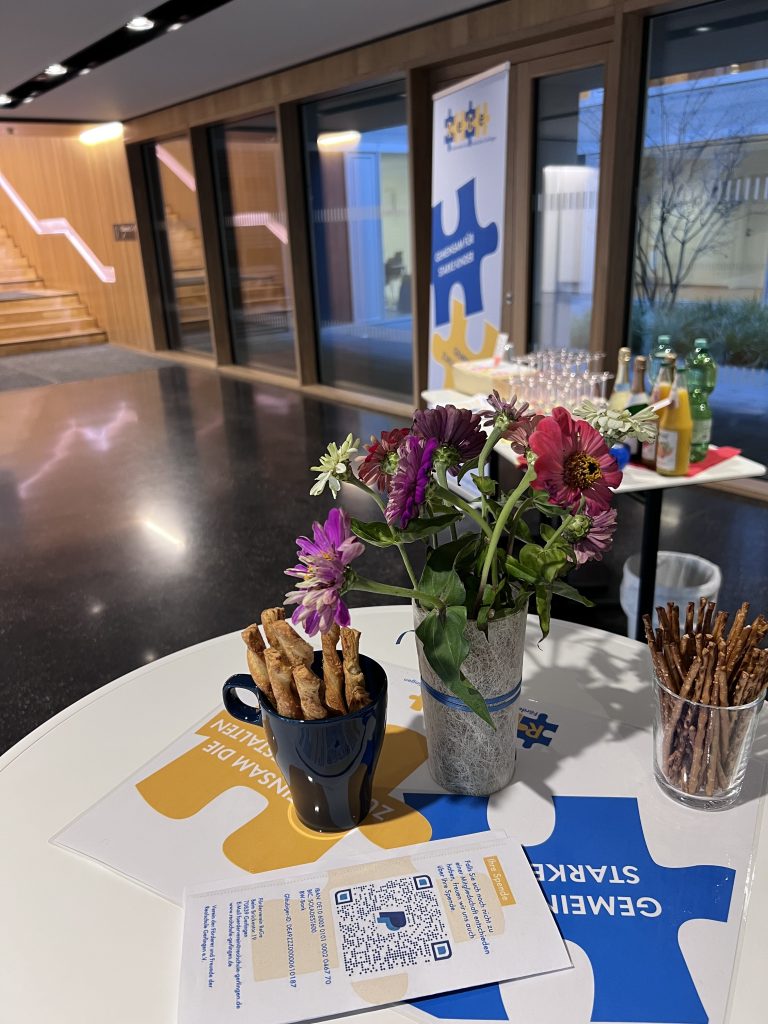 Ein Stehtisch, auf dem in einer Vase Blumen stehen und Infomaterial des Fördervereins liegt.